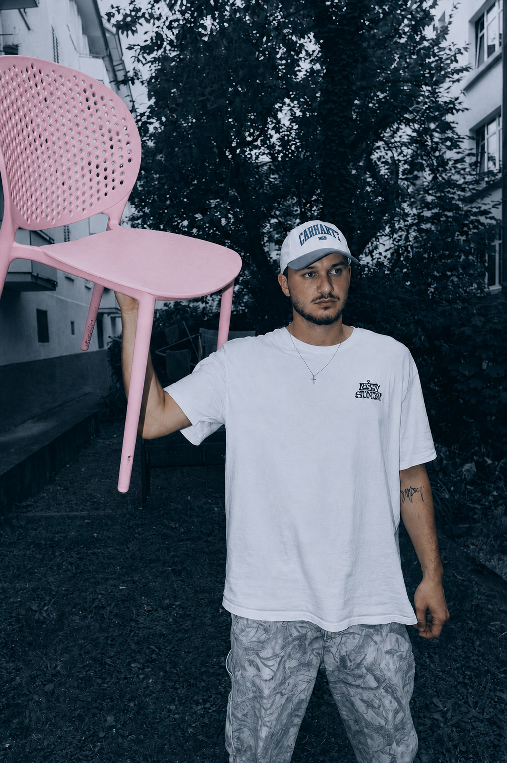 :DARREN portrait — white tee, cap, holding a pink chair
